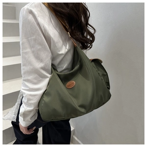 Détail d'un sac à bandoulière en nylon vert foncé avec un patch logo en cuir marron