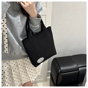 Detail view of the black corduroy fabric texture and minimalist brand logo on the tote bag