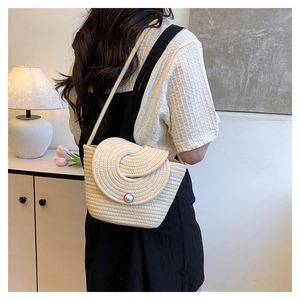 Detail of cream woven shoulder bag featuring a circular flap and a large pearl accent