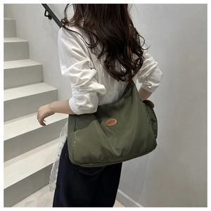 Sac bandoulière en nylon vert olive avec patch en cuir porté par un mannequin en escalier