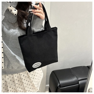 Detail of black corduroy tote bag showing vertical texture and white logo label