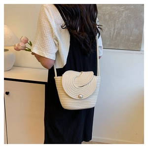 Close-up of handmade woven straw bucket bag with elegant spiral lid and pearl closure