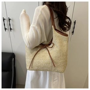 Close-up of beige woven straw tote bag with brown leather bow and shoulder straps