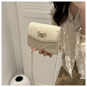 Detail of straw woven crossbody bag featuring a golden bow buckle and fine texture