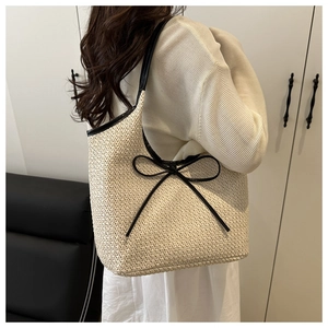 Detail of woven straw tote bag featuring black leather bow and elegant shoulder strap design