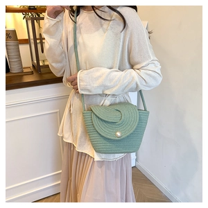 Detail of mint green woven crossbody bag with pearl clasp and braided strap worn by model