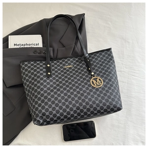 Detail der schwarzen Monogramm-Tote-Bag mit goldener M-Anhänger und Ledergriffen im Büro