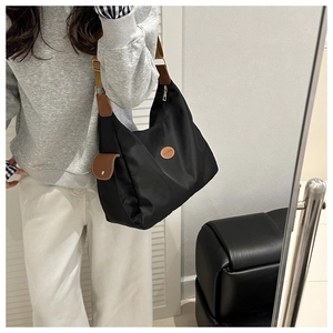 Detail of waterproof black nylon hobo bag with brown leather accents and wide shoulder strap