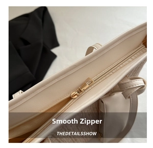 Detailed close-up of premium gold zipper closure on beige woven straw tote bag