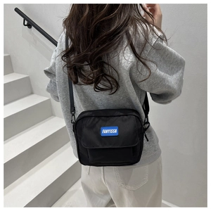 Detail of minimalist black nylon crossbody bag with blue logo on modern white stairs