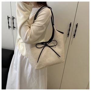 Detail of woven straw tote bag with black leather trim and large decorative bow on model