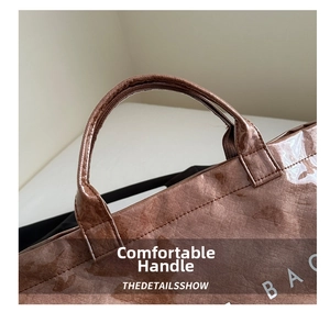 Detail of reinforced brown tote handle and crinkled glossy leather texture