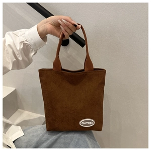 Detail of brown corduroy tote bag showing ribbed texture and brand label in urban setting