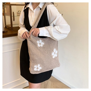 Detail of hollow crochet straw tote bag featuring white floral patterns and shoulder strap