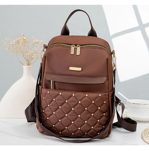 Close-up of brown quilted nylon backpack with gold rivets on white marble table