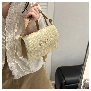 Detail of straw woven crossbody bag featuring a golden bow accent and leather strap