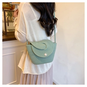 Close-up of light green woven bucket bag featuring a large pearl clasp and rope texture