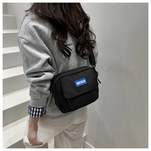Gros plan sur le sac bandoulière noir avec étiquette bleue FANYISSA porté par un modèle