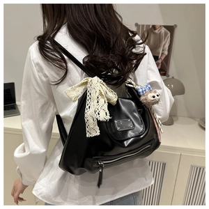 Detail einer schwarzen PU-Ledertasche mit einer Spitzenschleife und Affen-Plüschanhänger
