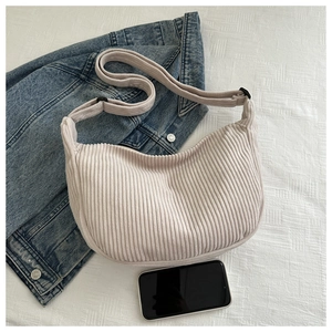 Detail view of beige corduroy crescent shoulder bag with wide strap and phone for scale