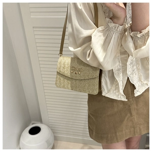 Detail of straw woven crossbody bag with golden metal bow and brown shoulder strap