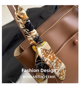 Detail of silk twilly scarf with carriage print wrapped on a brown leather bag handle