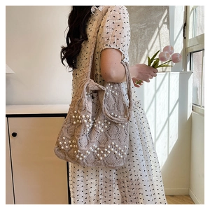Close-up of beige knitted tote bag with white pearl wave patterns in natural light