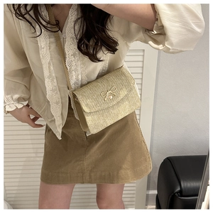 Detail of straw woven crossbody bag with golden bow buckle and pearl accent on model