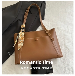 Detail of a brown tote bag with silk scarf handle next to a smartphone for size reference