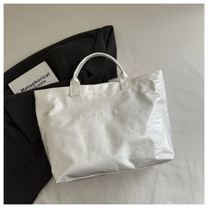 Detail of white glossy leather tote bag with embossed TOTE BAG text and crinkle texture