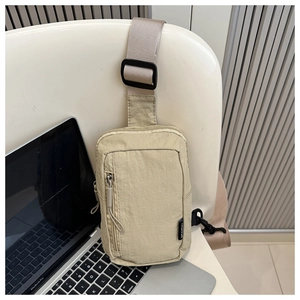 Detail view of light khaki nylon chest bag with zippers beside a laptop on a chair