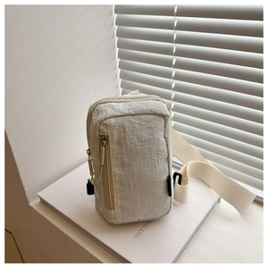 Detail of beige wrinkled texture crossbody chest bag placed on a white book decor