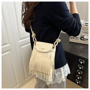 Détail du petit sac bandoulière à franges crème porté par un mannequin en intérieur