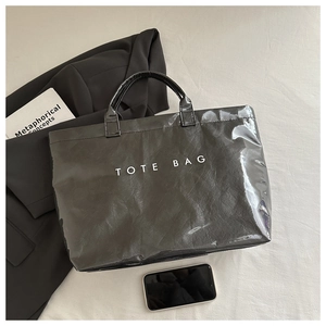 Close-up of black glossy tote bag with white text and textured finish on a styled surface