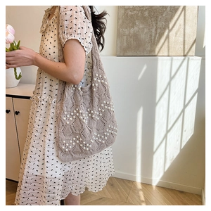 Model wearing a beige knitted tote bag with white faux pearl embellishments and V-pattern