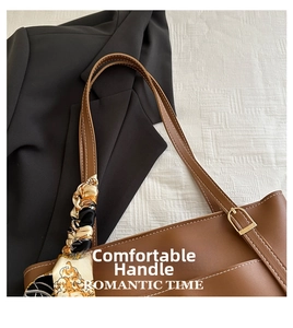 Close-up of brown leather tote bag with white stitching and decorative silk scarf handle