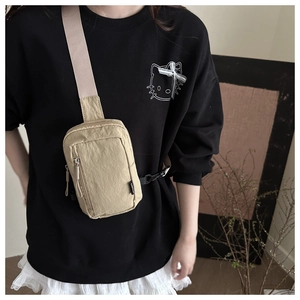 Close-up of a beige nylon crossbody chest bag worn by a model in casual streetwear