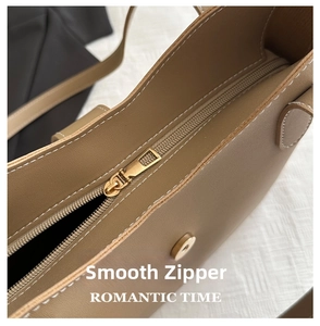Detail of brown leather tote bag with white contrast stitching and gold metal zipper