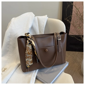 Detail of brown tote bag with white contrast stitching and a patterned silk scarf handle