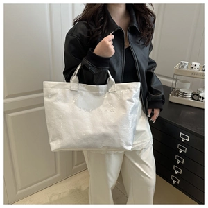 White glossy tote bag detail with TOTE BAG embossed text and minimalist handle design