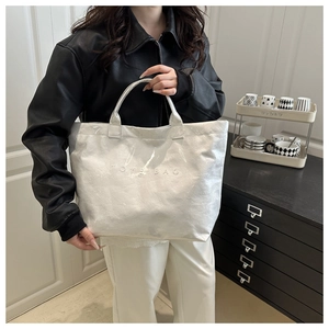 Close-up of white tote bag with TOTE BAG embossed text and durable handles