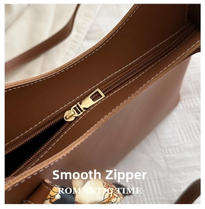 Détails du zip doré et des surpiqûres sur un sac cabas en cuir marron avec foulard soie