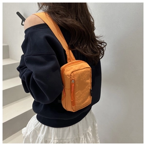 Model wearing vibrant orange nylon mini crossbody bag with wide shoulder strap