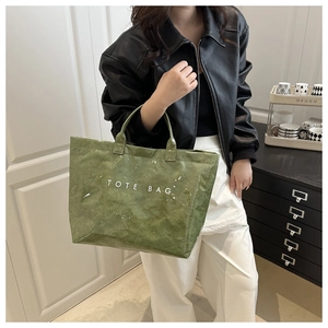 Detail of green textured tote bag with white text print shown on a model's shoulder