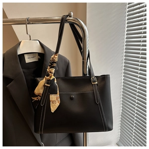 Detail of black leather tote bag with white stitching and decorative floral scarf