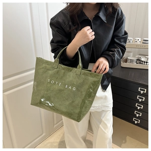 Detail of green glossy crinkled tote bag with white text held by model in leather jacket