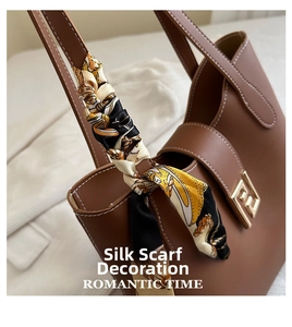 Close-up of brown leather handbag featuring printed silk scarf handle and gold metal clasp