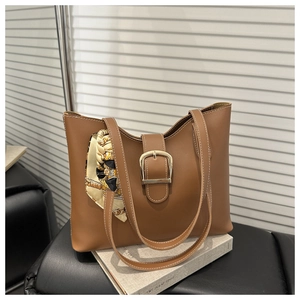 Close-up of brown leather tote bag with gold buckle, contrast stitching and silk scarf decoration