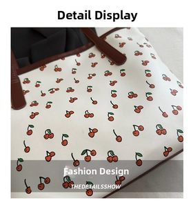 Détail d'un sac cabas blanc à imprimé cerise et anse en cuir marron avec surpiqûres