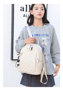 Detail of off-white quilted backpack with gold studs and a cute black bear pendant